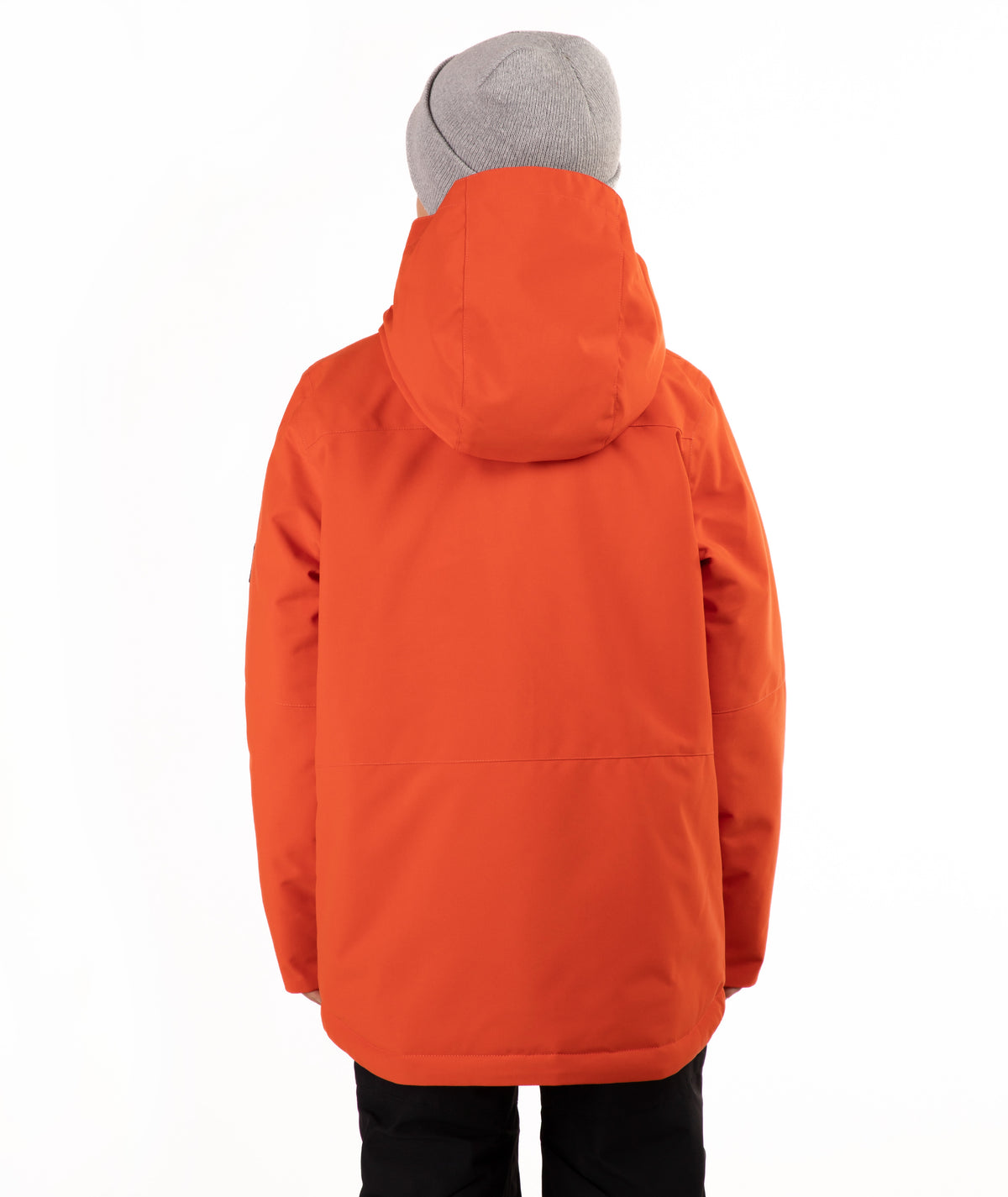 A young boy wearing a bright orange hooded snowboard jacket, a gray knit beanie, and black pants, standing against a plain white studio background.