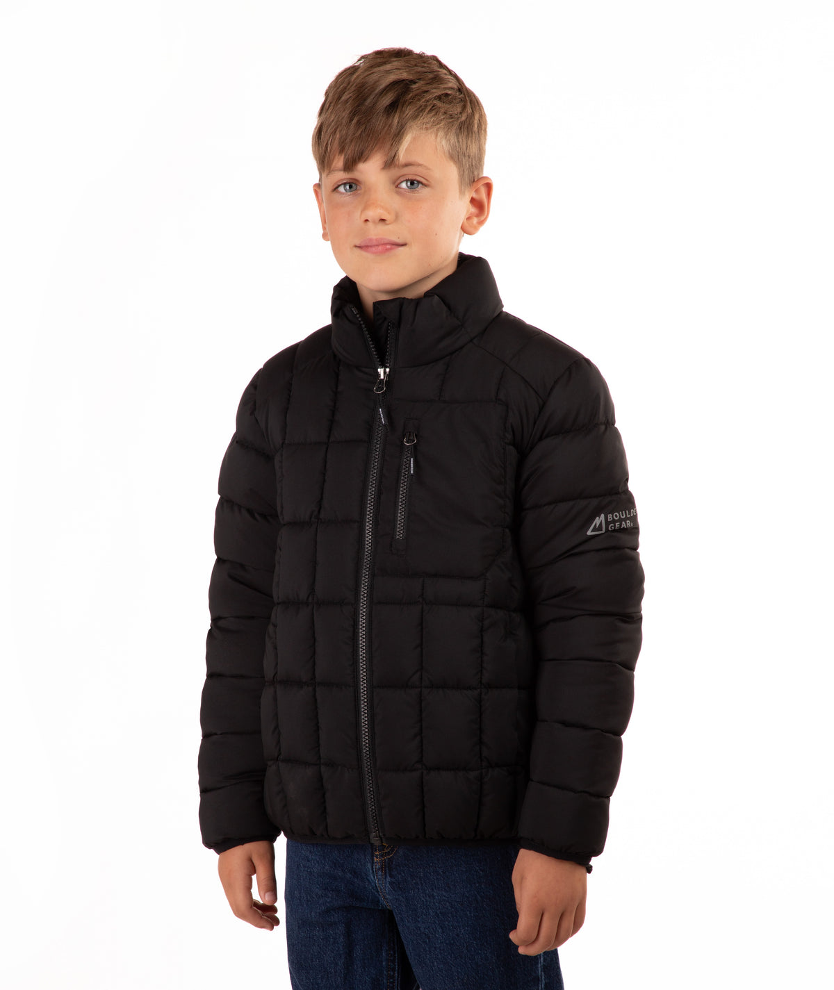 A young boy wearing a black quilted puffer jacket with a stand-up collar and front zipper, paired with blue jeans, photographed against a solid white background.