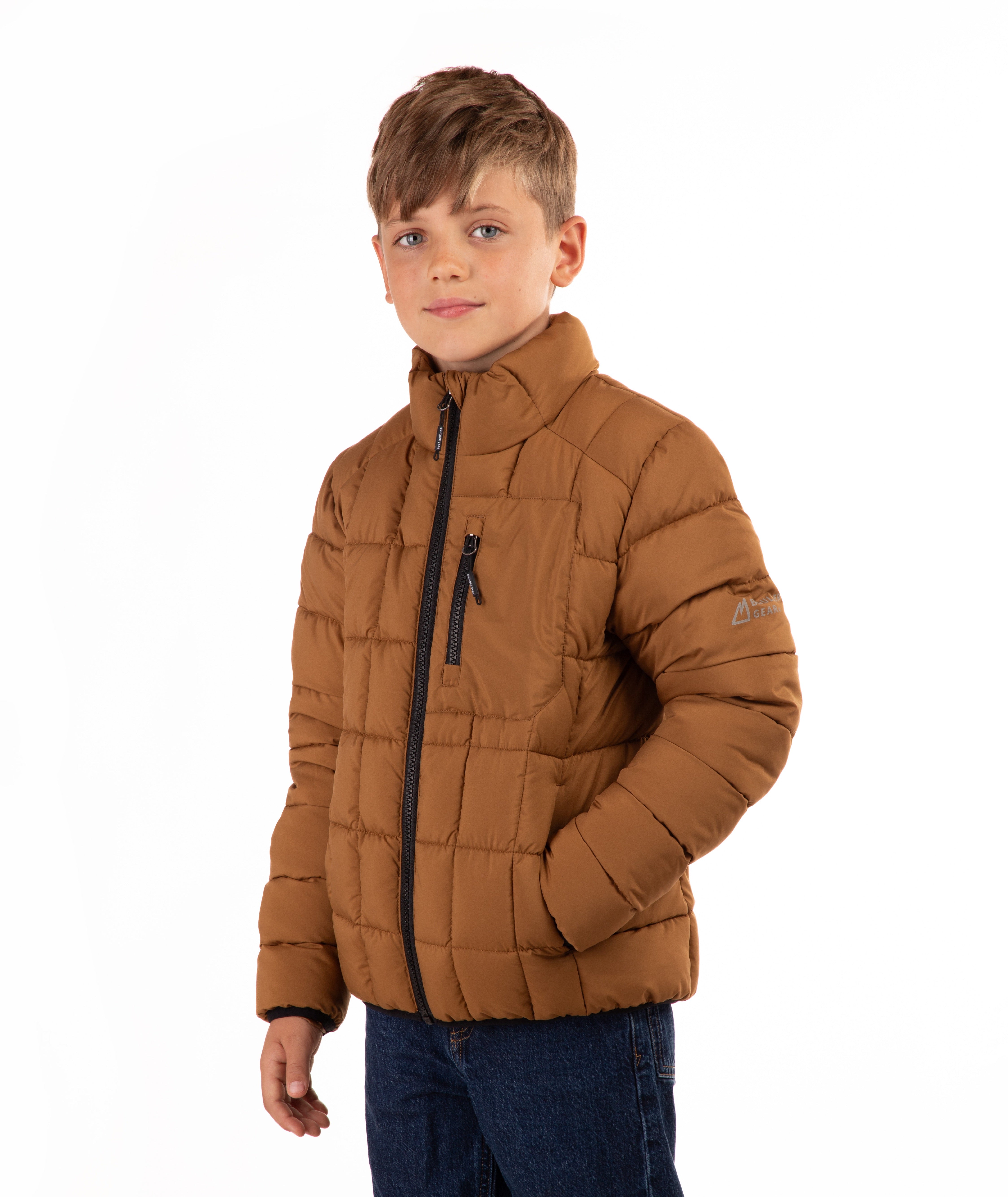 A young boy wearing a brown puffer jacket with black zippers and blue jeans, standing against a plain white background.