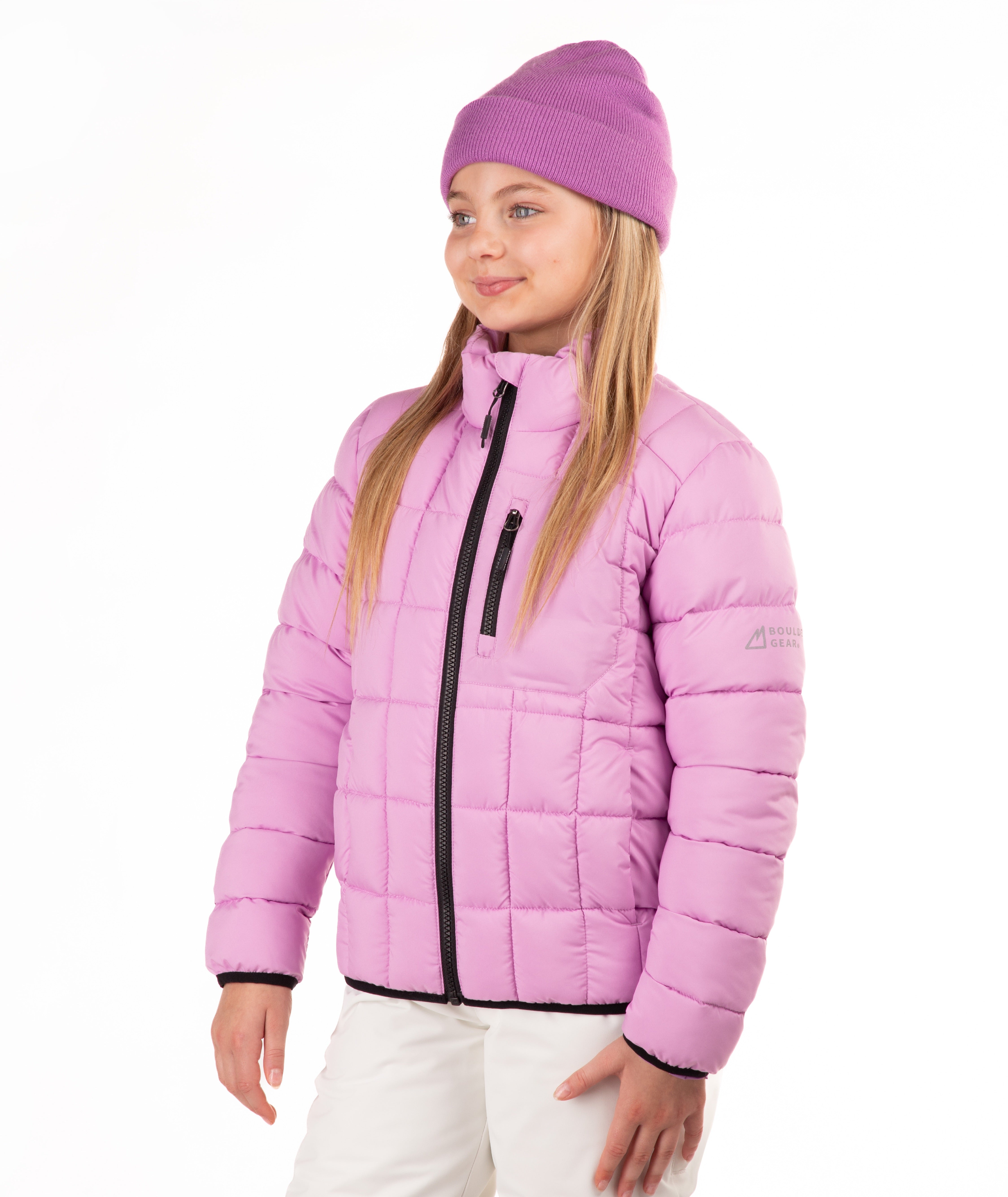 A young girl wearing a light purple puffer jacket, a matching pink knit beanie, and white pants, standing against a plain white background.