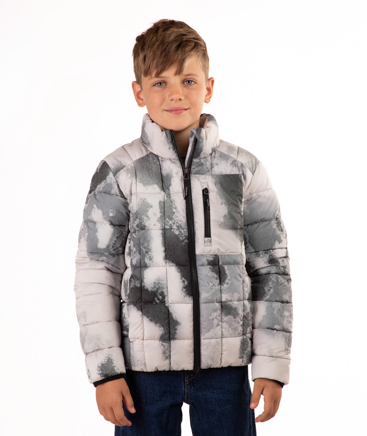 A young boy wearing a gray and white abstract patterned puffer jacket with a high collar and black zipper, paired with dark blue jeans, photographed against a solid white background.