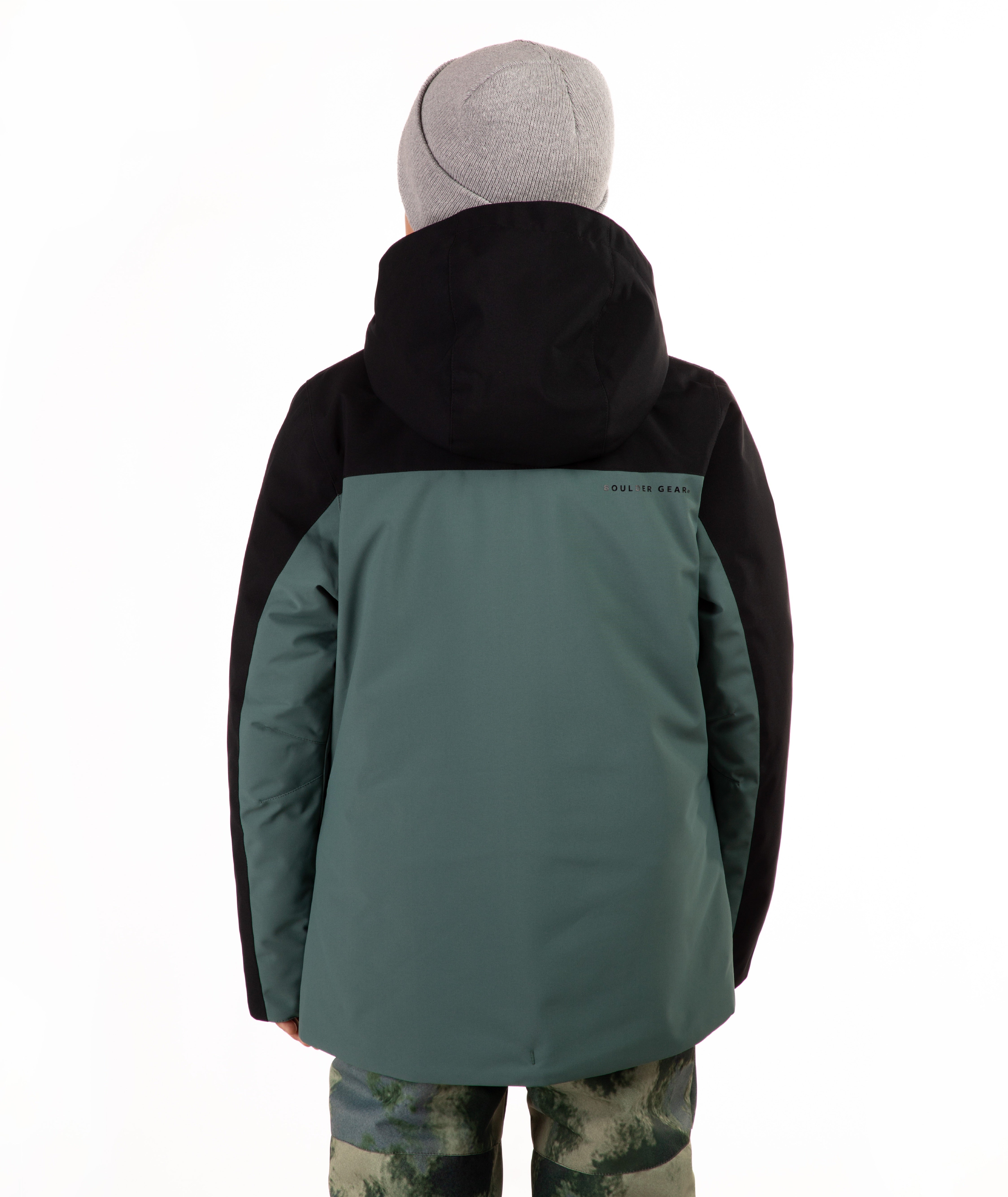 A child viewed from the back wearing a color-blocked ski jacket in black and muted teal, paired with a gray beanie and camouflage-patterned pants, against a plain white background.