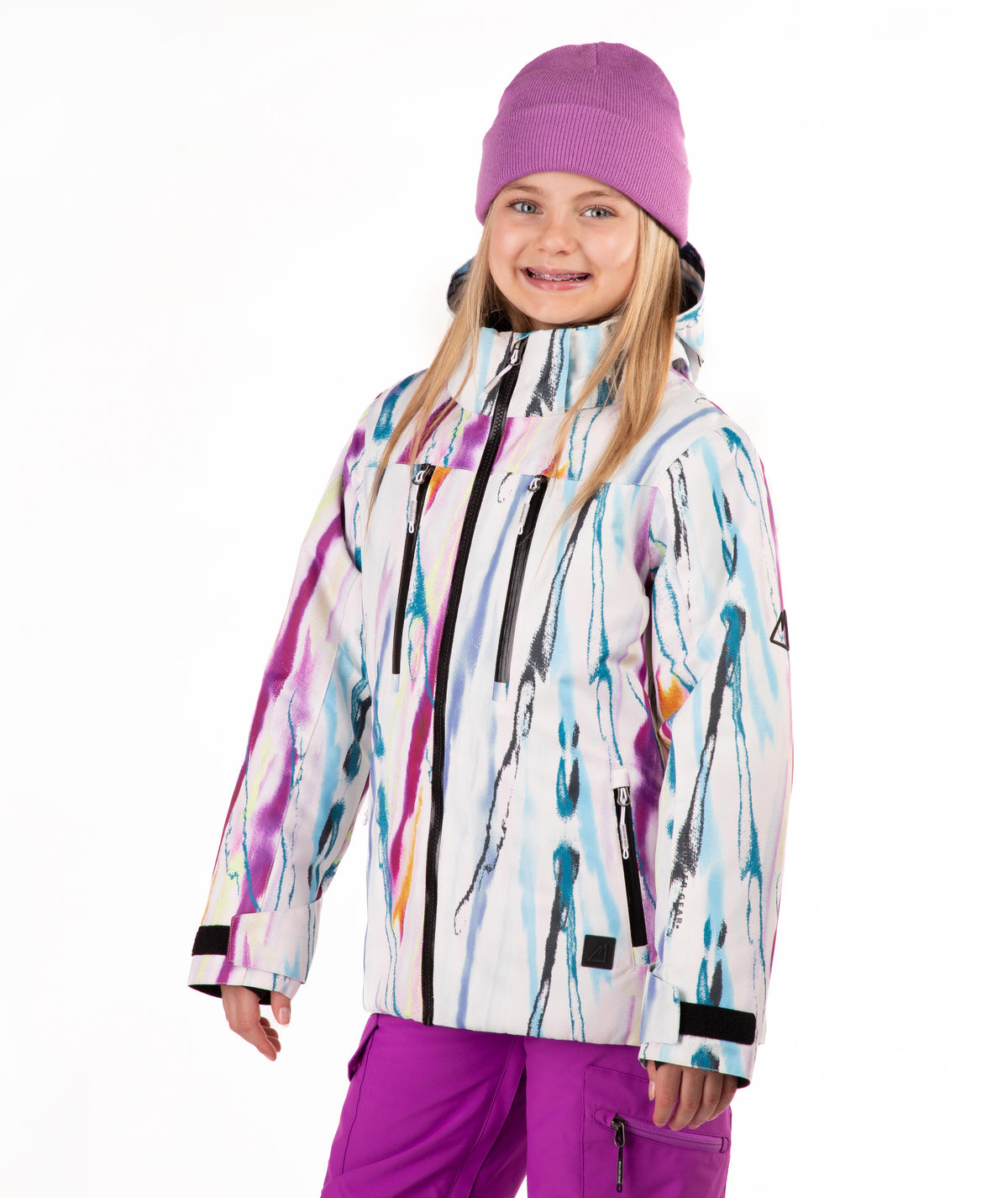 A child wearing a colorful abstract print ski jacket, a purple knit beanie, and purple ski pants, standing against a plain white studio background.