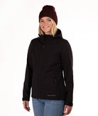 A woman wearing a black hooded jacket, a dark burgundy knit beanie, and blue jeans, standing against a plain white studio background.