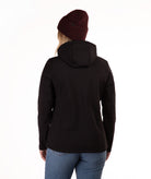 A woman viewed from the back wearing a black hooded jacket, a dark burgundy knit beanie, and blue jeans against a plain white studio background.
