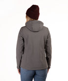 A woman viewed from the back wearing a dark gray hooded jacket, a burgundy knit beanie, and blue jeans against a plain white background.