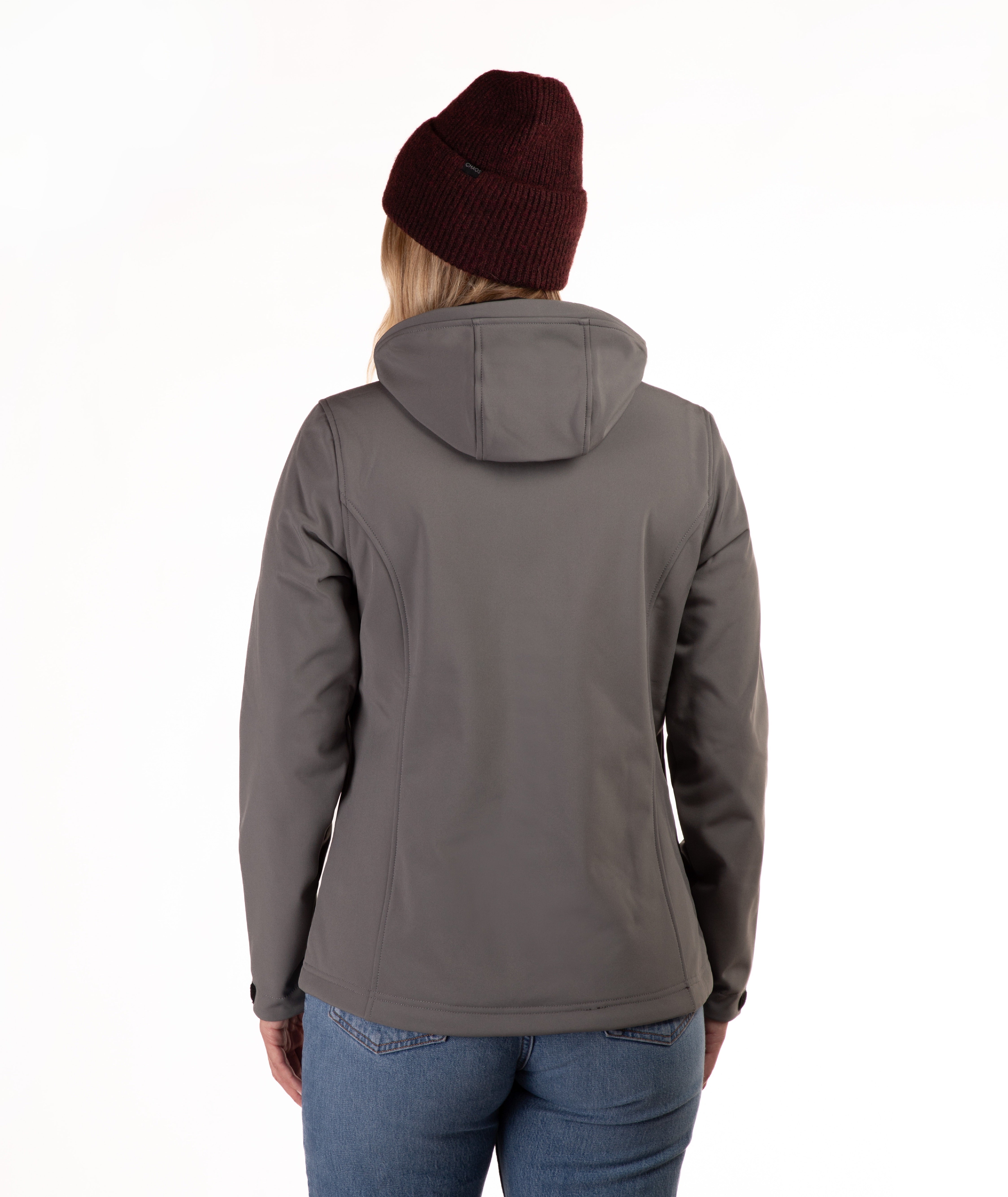 A woman viewed from the back wearing a dark gray hooded jacket, a burgundy knit beanie, and blue jeans against a plain white background.