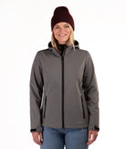 A woman wearing a gray hooded zip-up jacket, a dark red knit beanie, and blue jeans, standing against a plain white background.