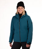 A woman wearing a teal insulated winter jacket with a black beanie and black pants, standing against a plain white studio background.