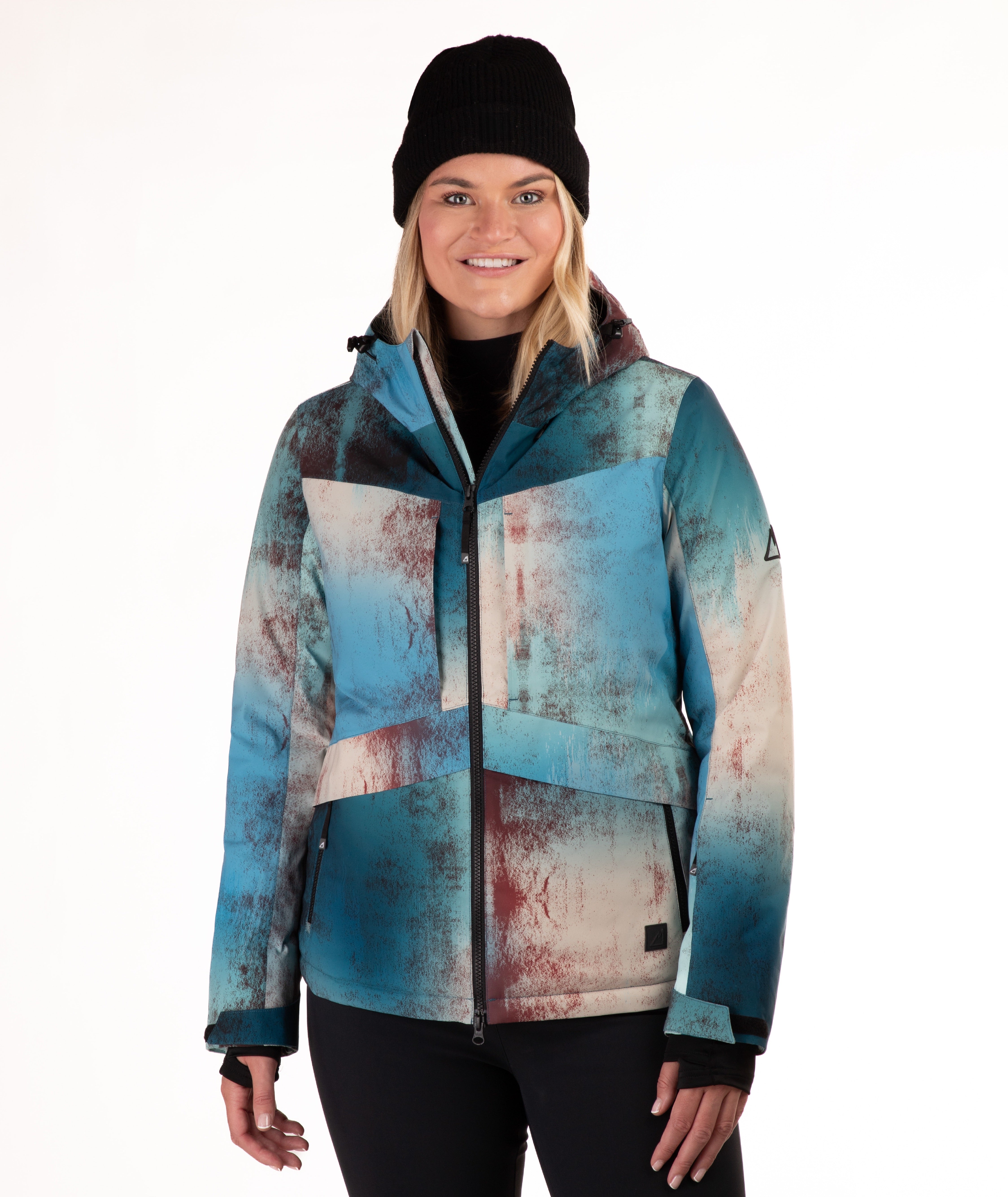 A woman wearing a blue and beige abstract-patterned ski jacket, a black beanie, and black pants, standing against a plain white background.