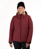 A woman wearing a dark red hooded ski jacket, a black knit beanie, and black pants, standing against a plain white studio background.