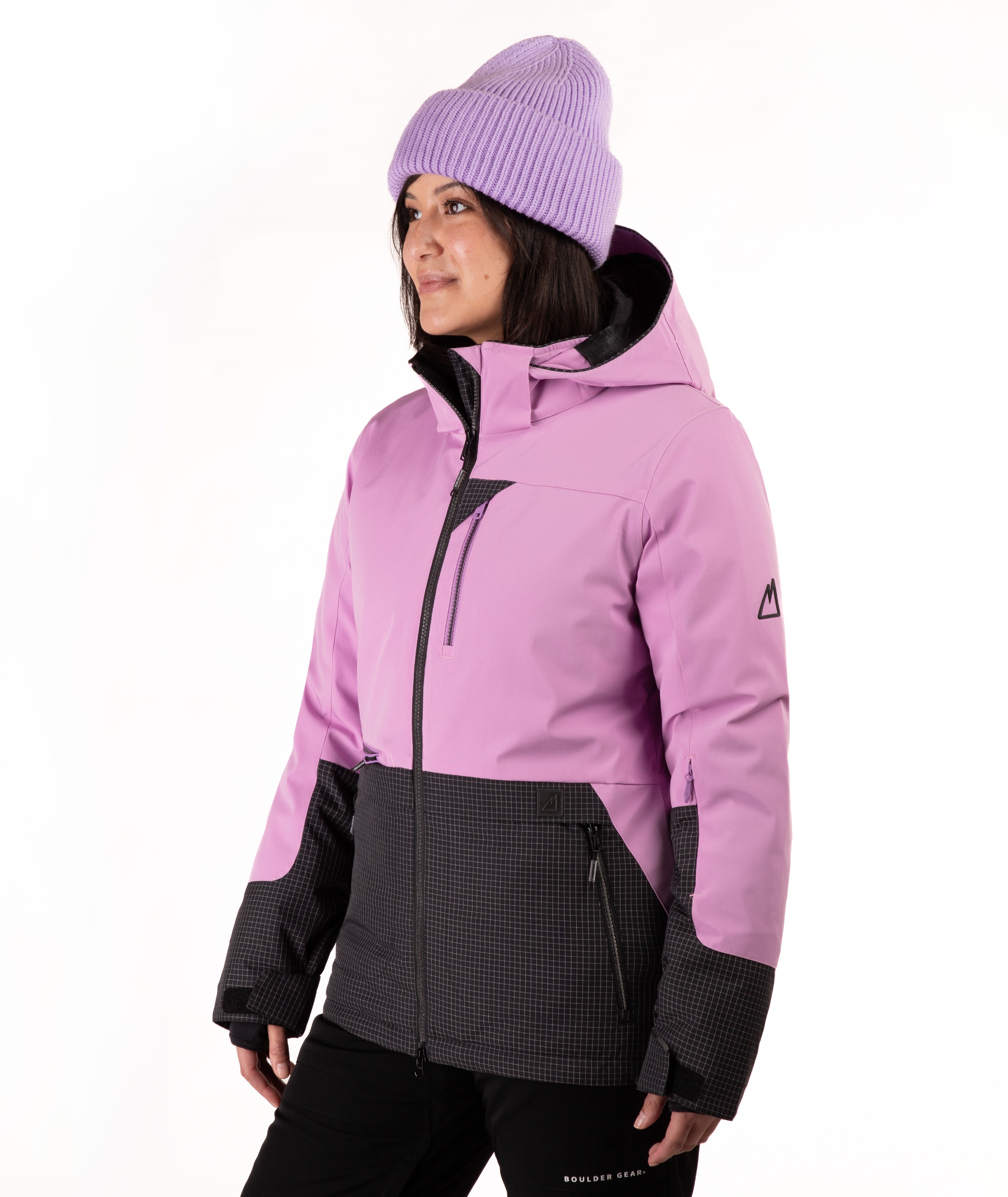 A woman wearing a light purple ski jacket with black accents, a matching purple knit beanie, and black ski pants, photographed against a plain white studio background.
