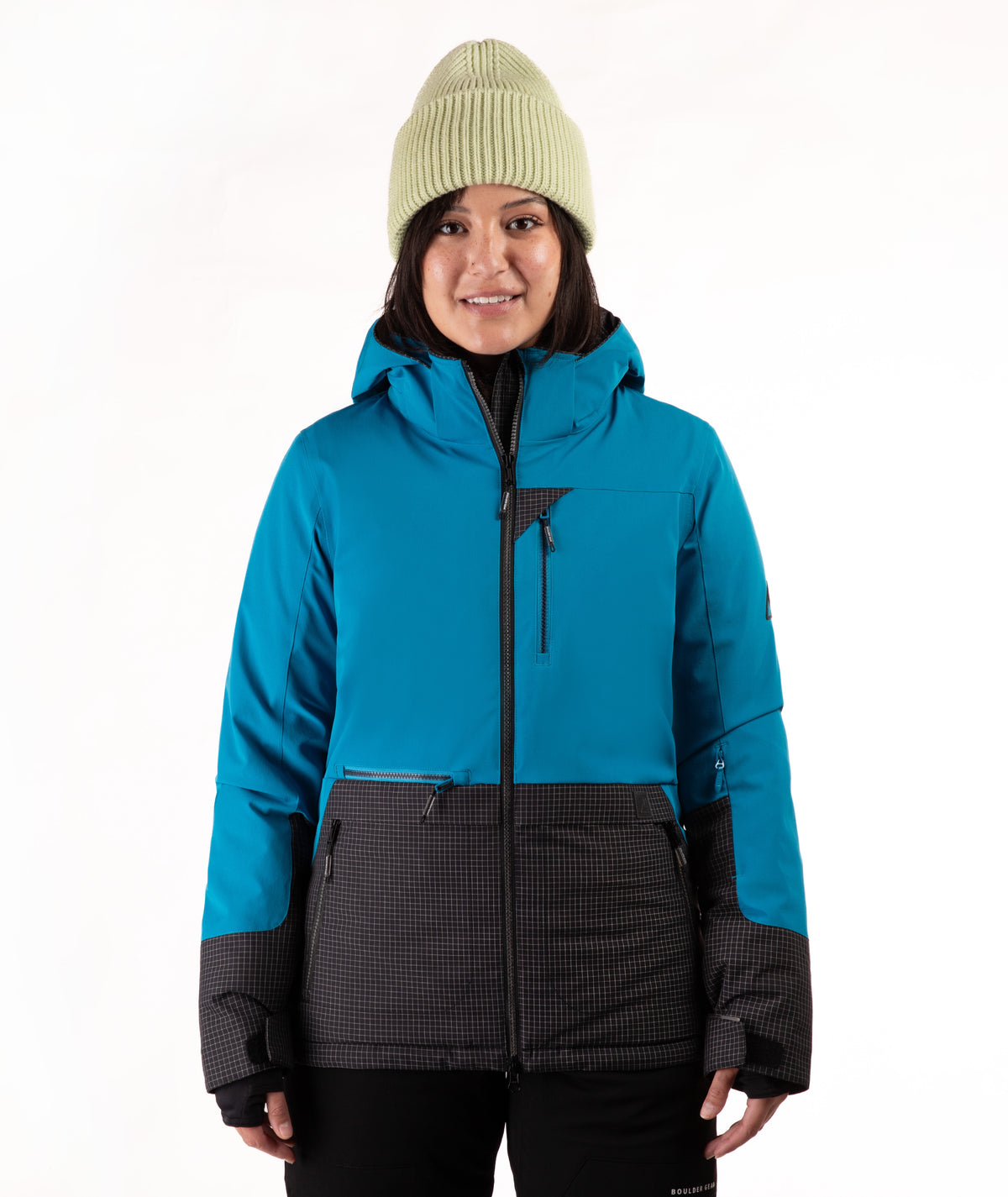 A woman wearing a bright turquoise and black check ski jacket with a green beanie, standing against a plain white background.