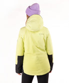 A person shown from the back wearing a light yellow hooded jacket with black check sleeve panels, a lavender knit beanie, and black pants against a plain white studio background.