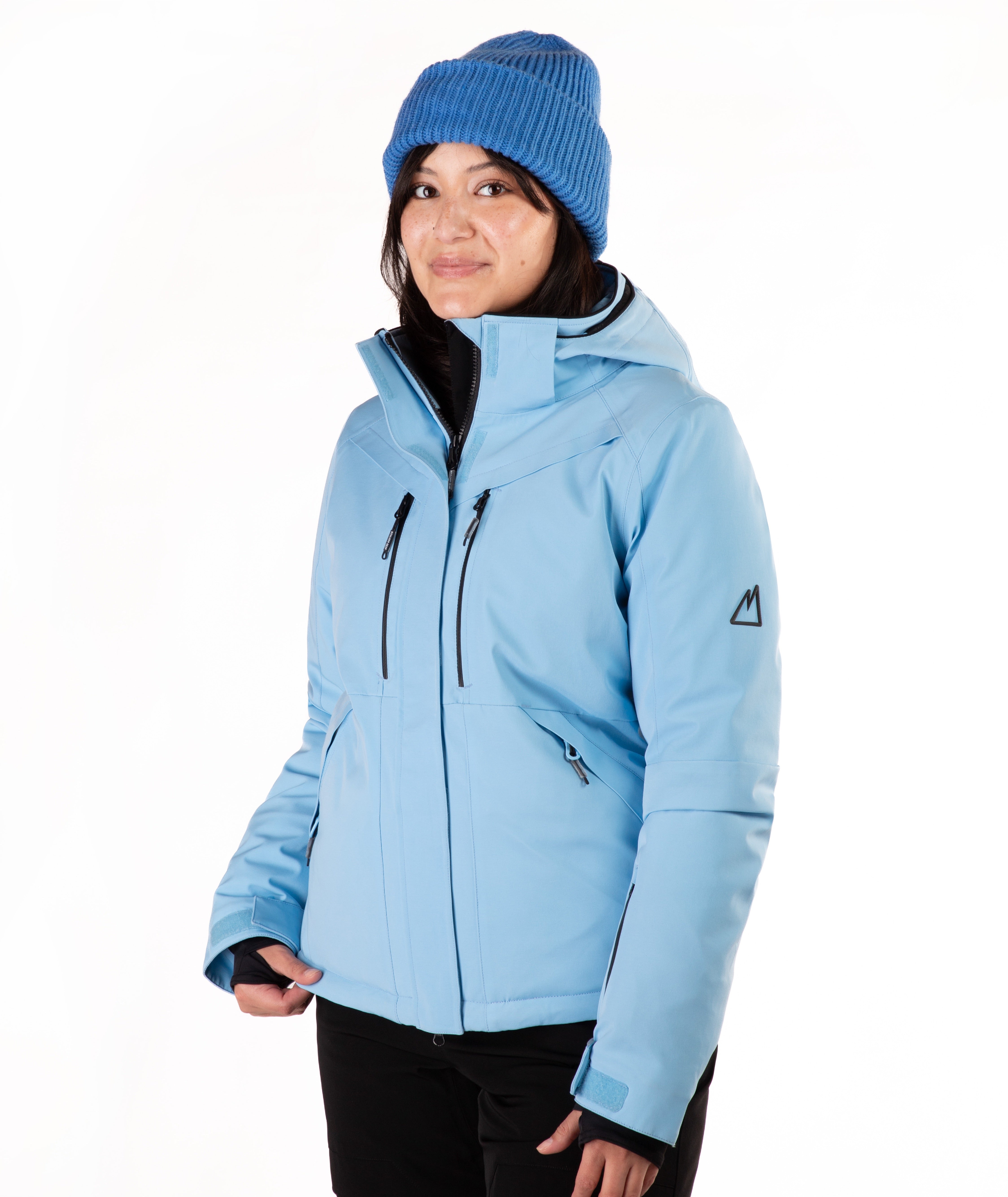 A woman wearing a light blue ski jacket and a matching knit beanie against a plain white studio background.