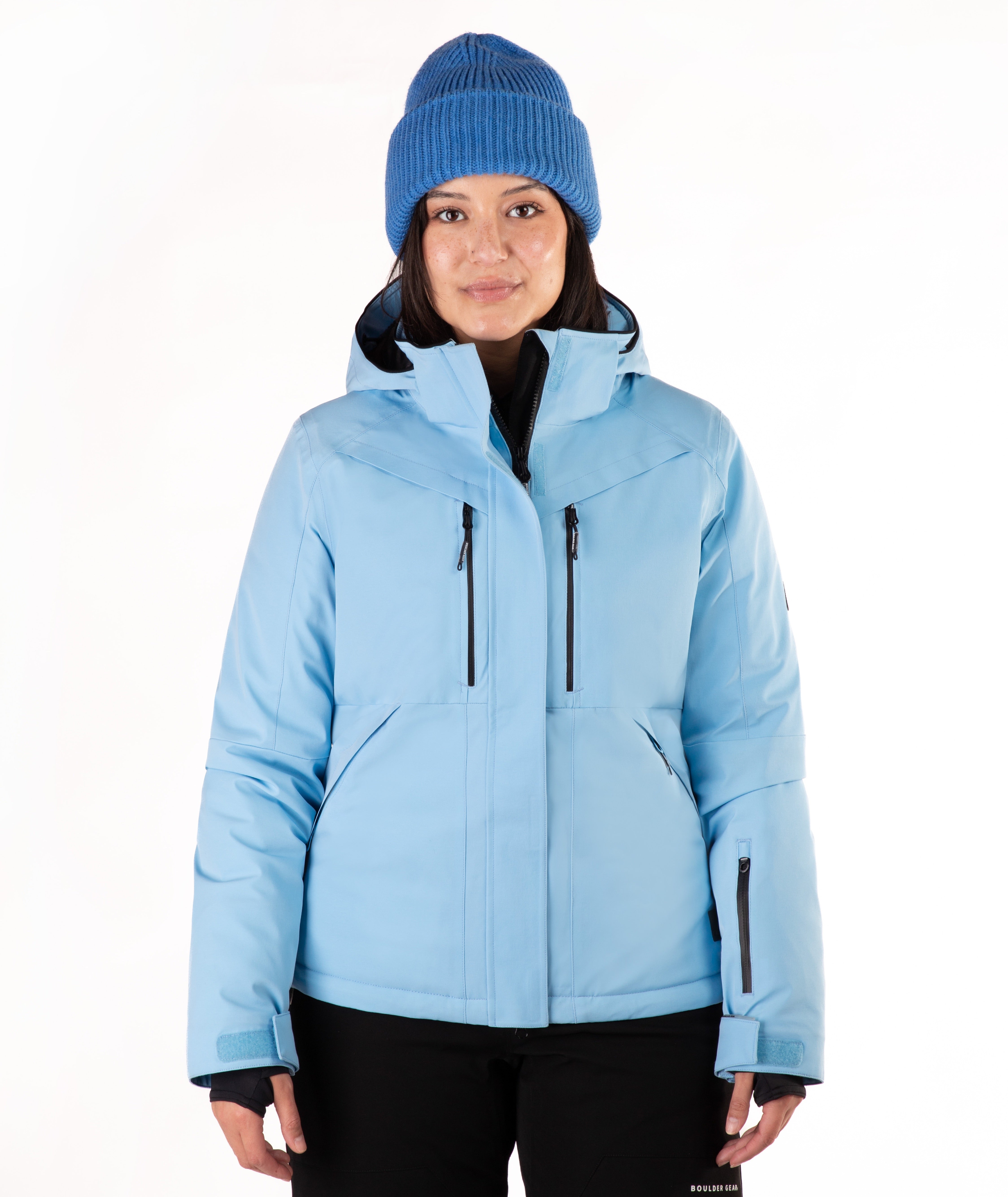 A woman wearing a light blue ski jacket and a matching knit beanie against a plain white studio background.