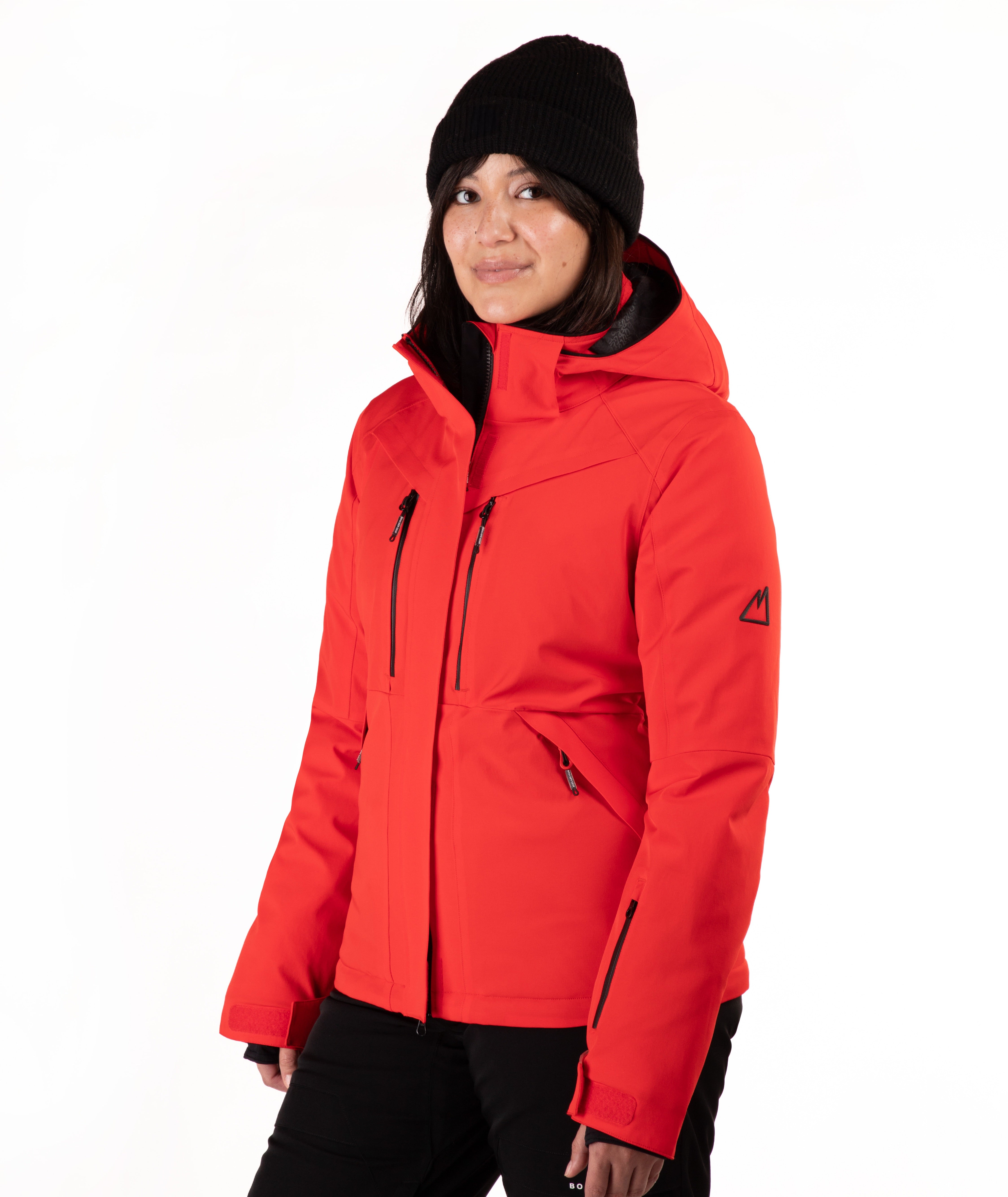 A woman wearing a bright red hooded ski jacket and a black knit beanie, standing against a plain white studio background.