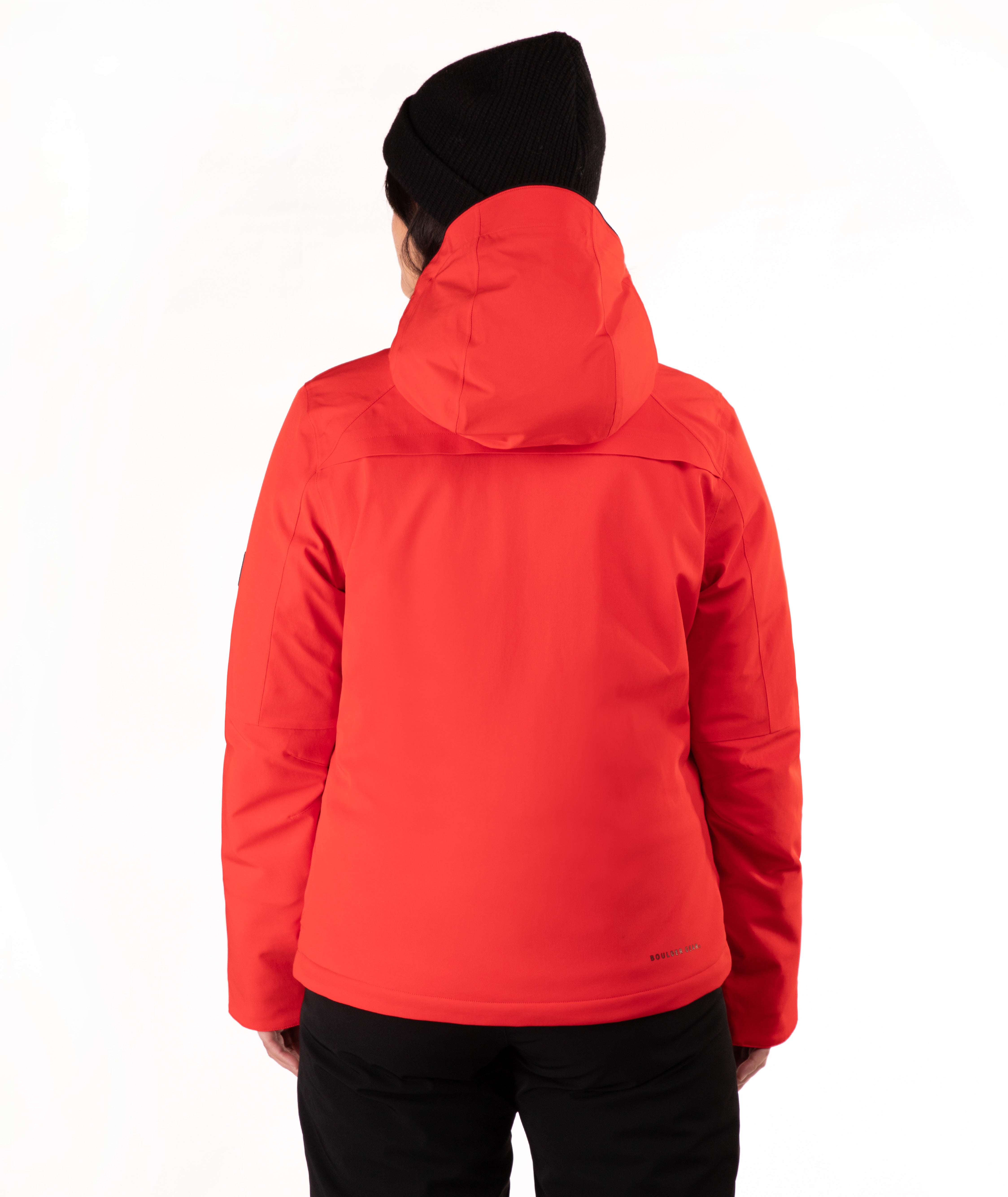 A woman wearing a bright red hooded ski jacket and a black knit beanie, standing against a plain white studio background.