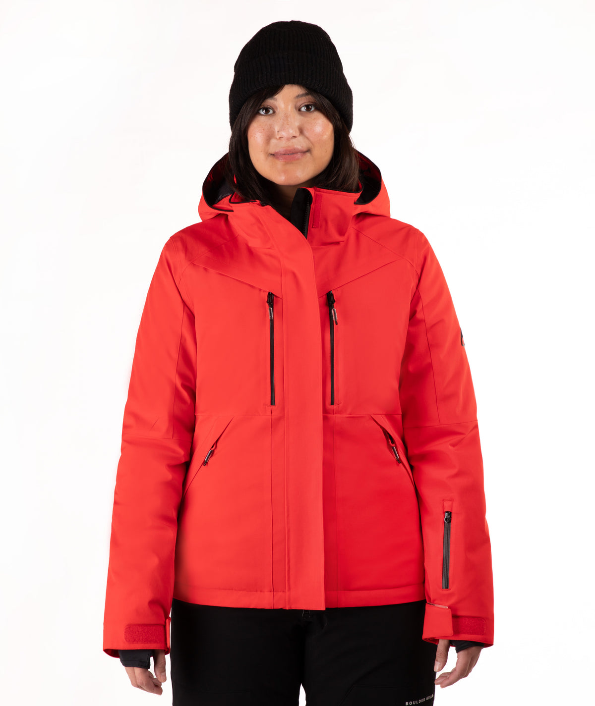 A woman wearing a bright red hooded ski jacket and a black knit beanie, standing against a plain white studio background.