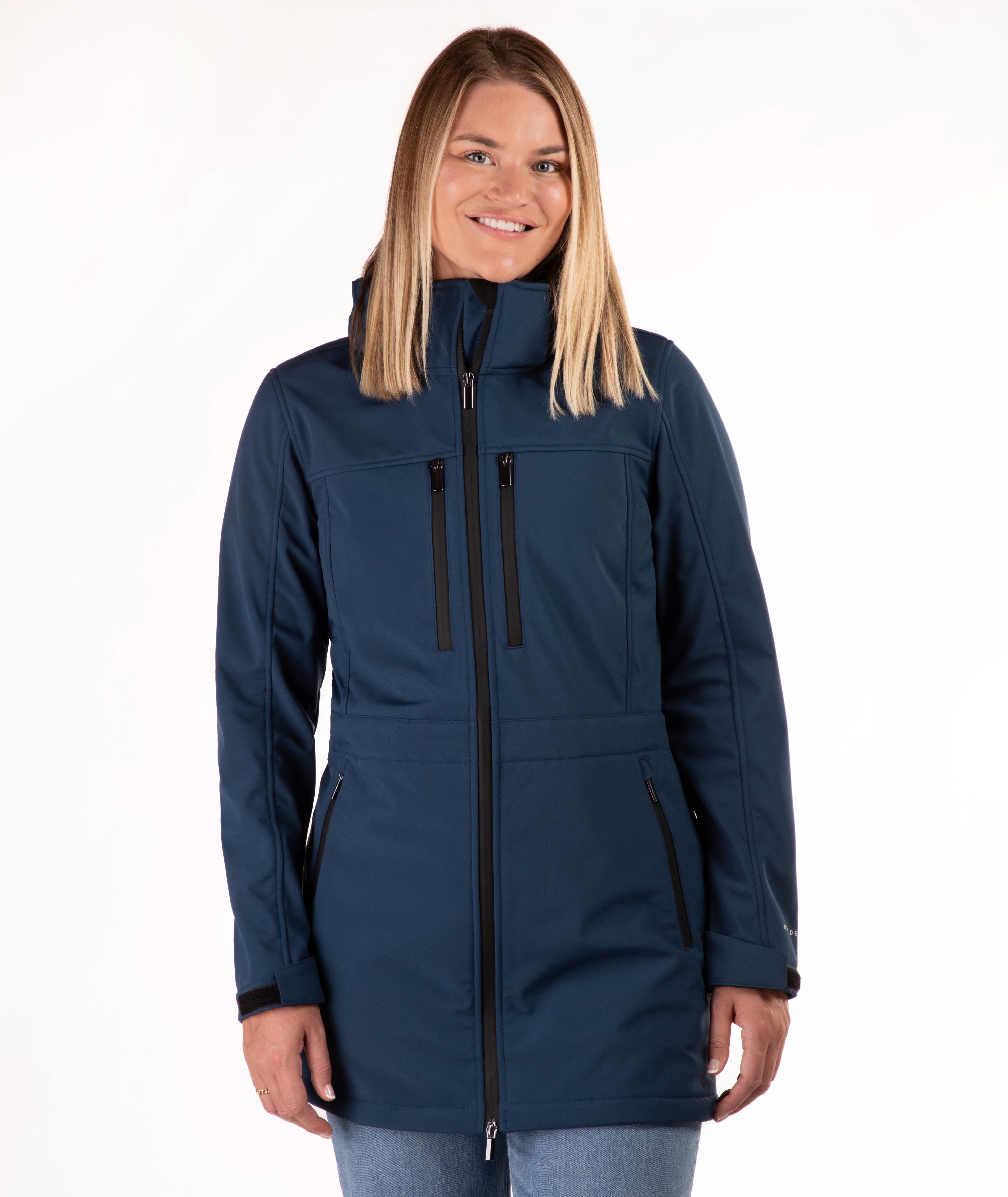 A woman modeling a navy blue hooded softshell jacket with black zippers, shown against a plain white studio background.