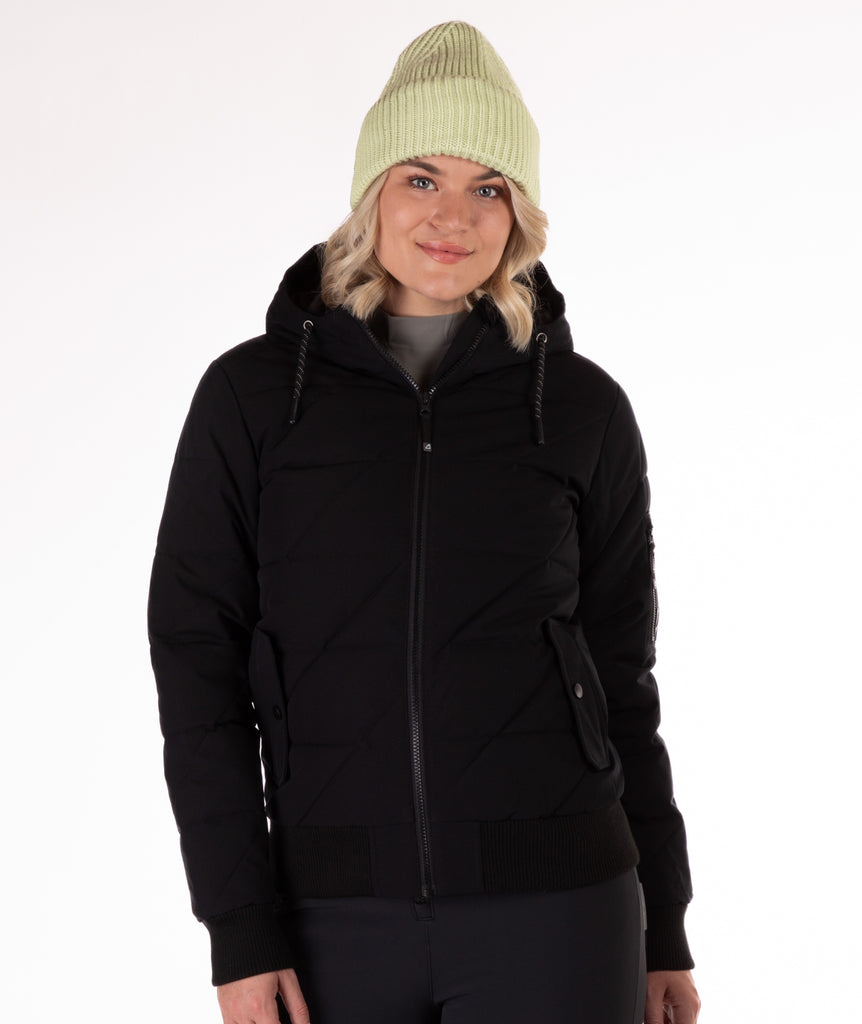 A woman wearing a black quilted jacket with a hood and black knit trim on wrist cuffs and hem on a white background