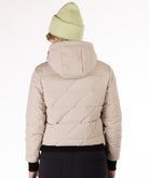 Beige quilted jacket with a hood worn by a person on a white background, back view of the jacket highlighting a Boulder Gear brand logo.