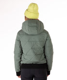 Woman wearing a green quilted jacket with a hood and black knit trim on wrist cuffs and hem on a white background.