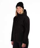 A woman wearing a black hooded jacket and a black knit beanie, photographed against a plain white studio background.