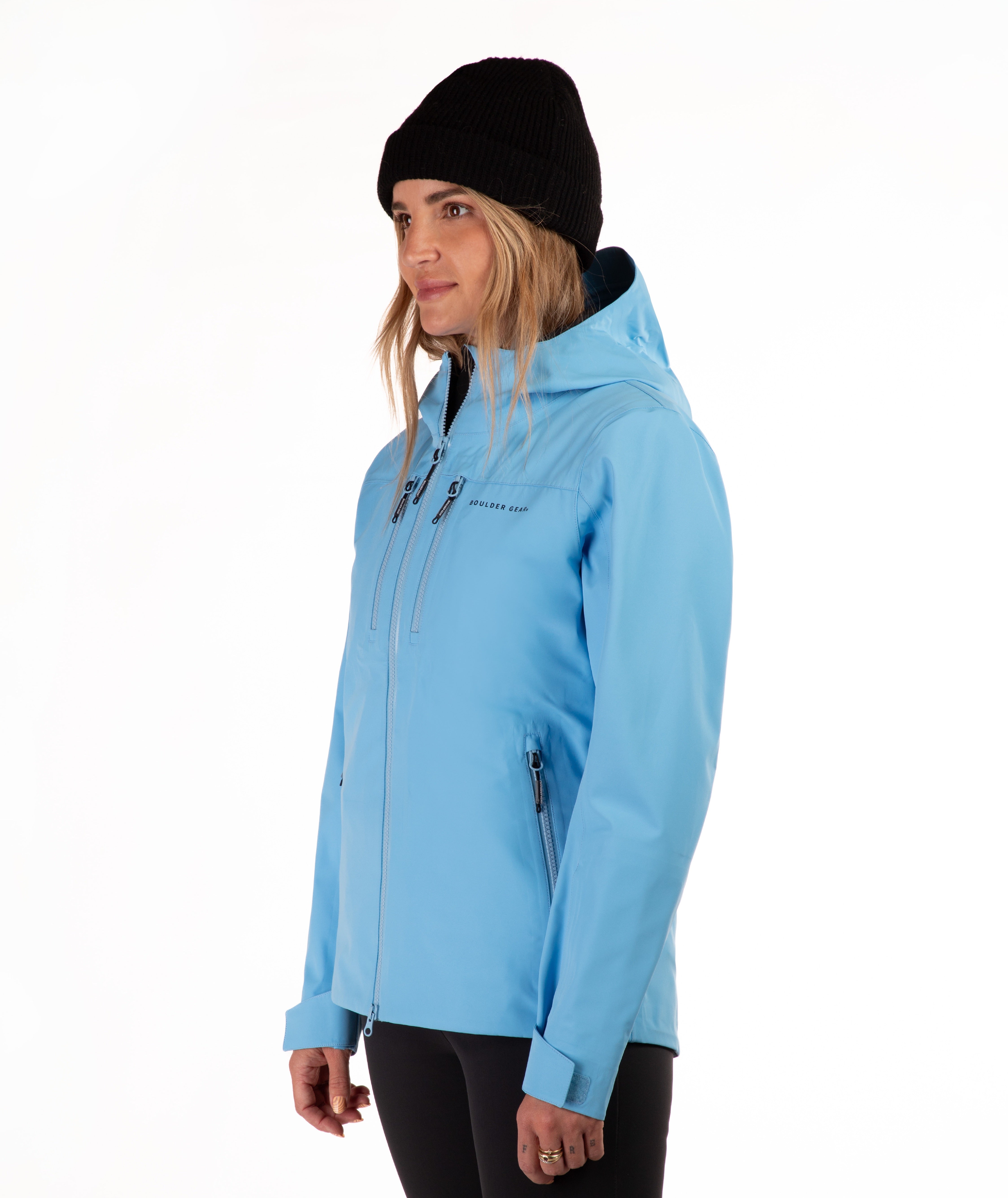 A woman wearing a light blue hooded ski jacket and a black beanie, shown in profile against a plain white studio background.