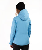 A woman wearing a light blue hooded ski jacket and a black beanie, shown from the back against a plain white studio background.