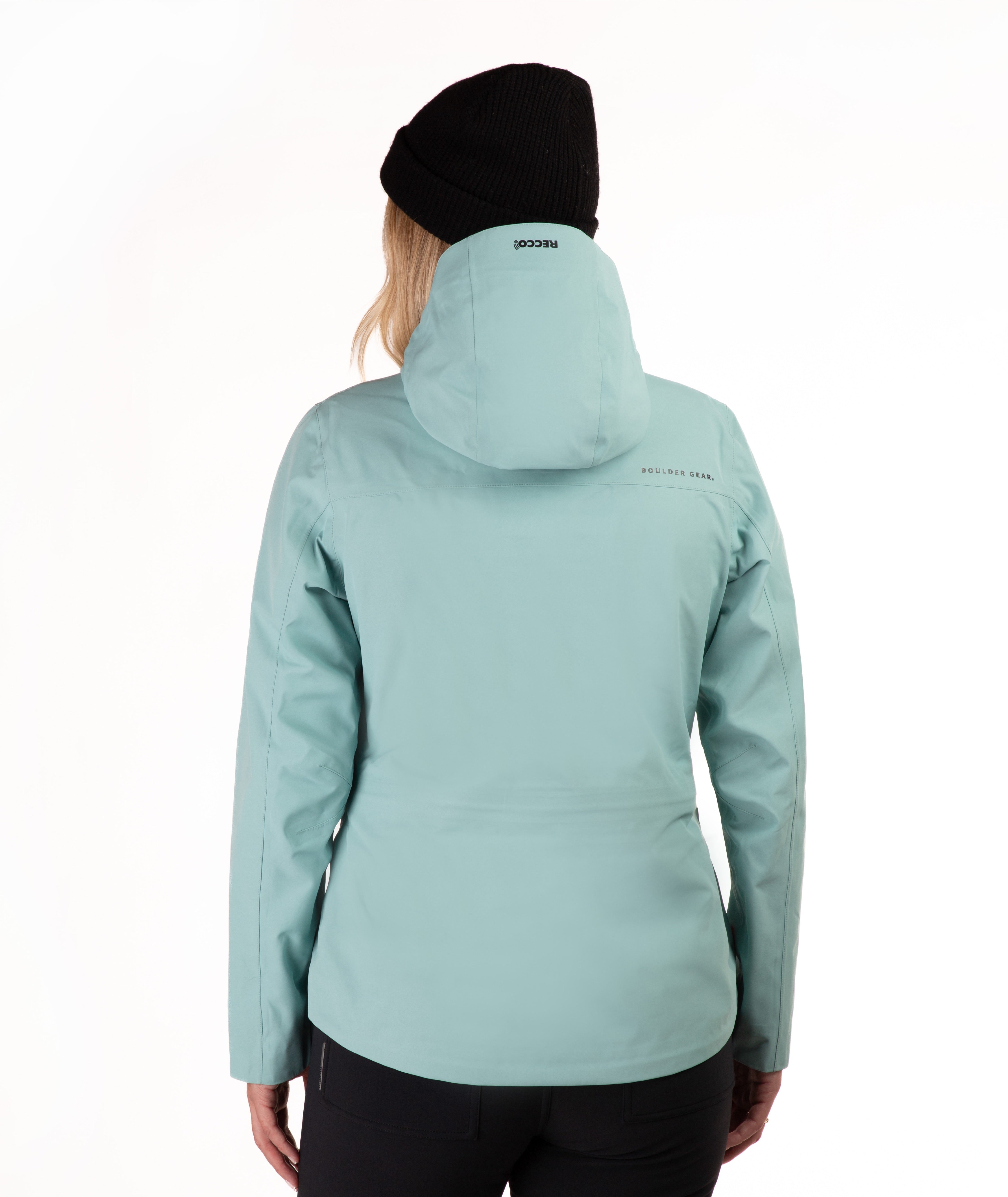 A woman wearing a light teal hooded ski jacket and black pants, paired with a black beanie, photographed against a plain white studio background.