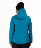 A woman viewed from the back wearing a bright teal hooded jacket and a black beanie against a plain white studio background.