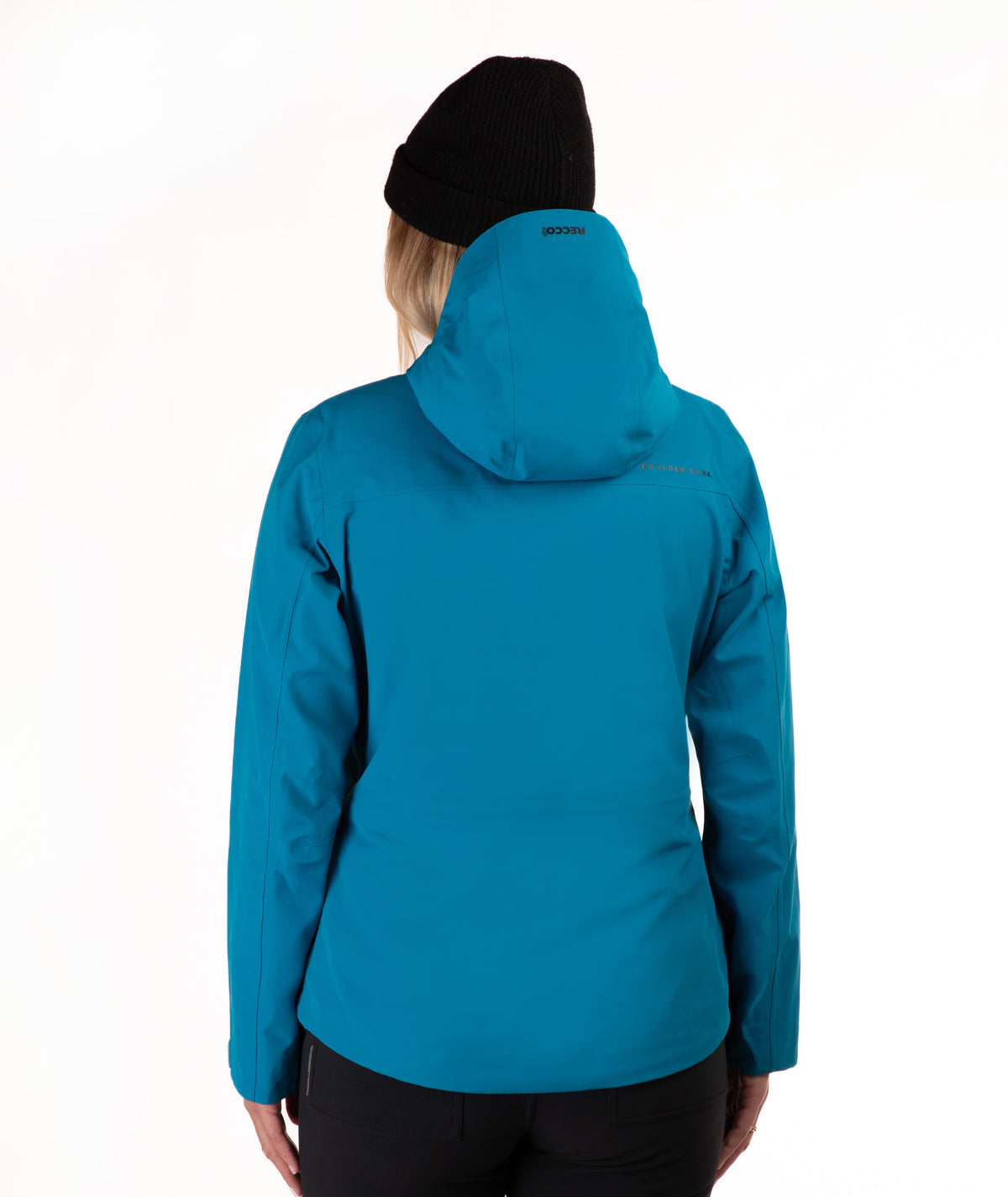 A woman viewed from the back wearing a bright teal hooded jacket and a black beanie against a plain white studio background.