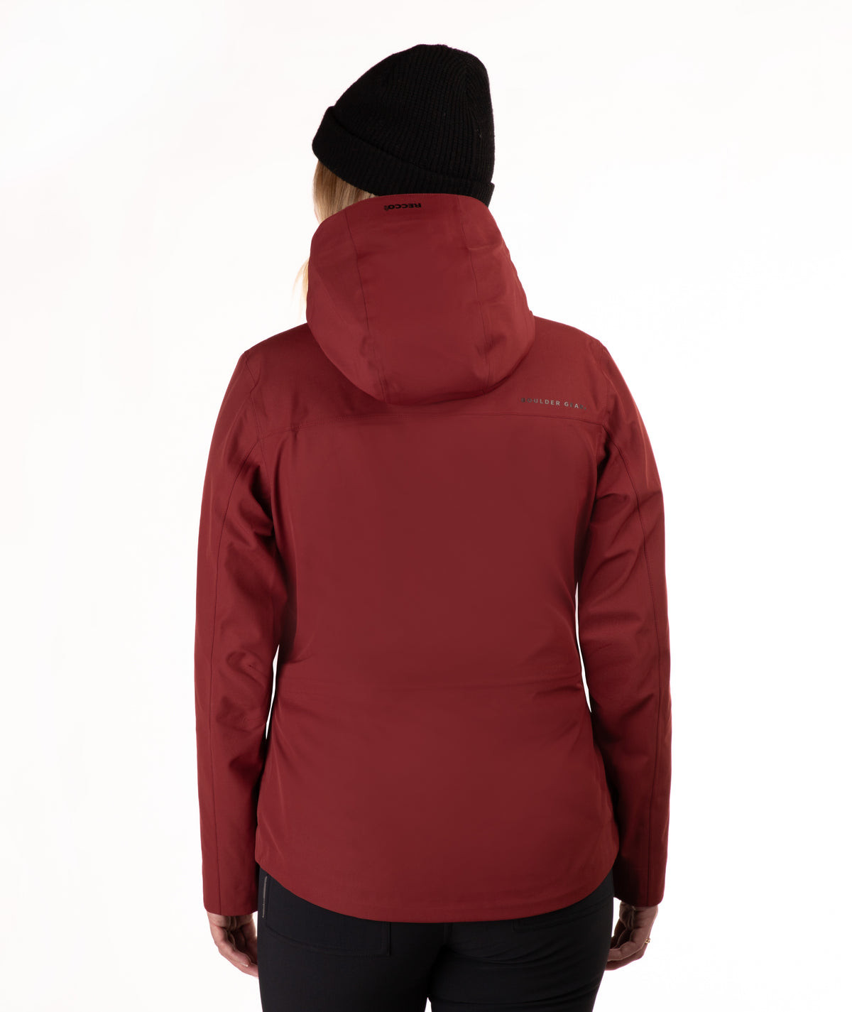 A person shown from the back wearing a hooded jacket in a deep burgundy red, a black beanie, and black pants against a plain white studio background.