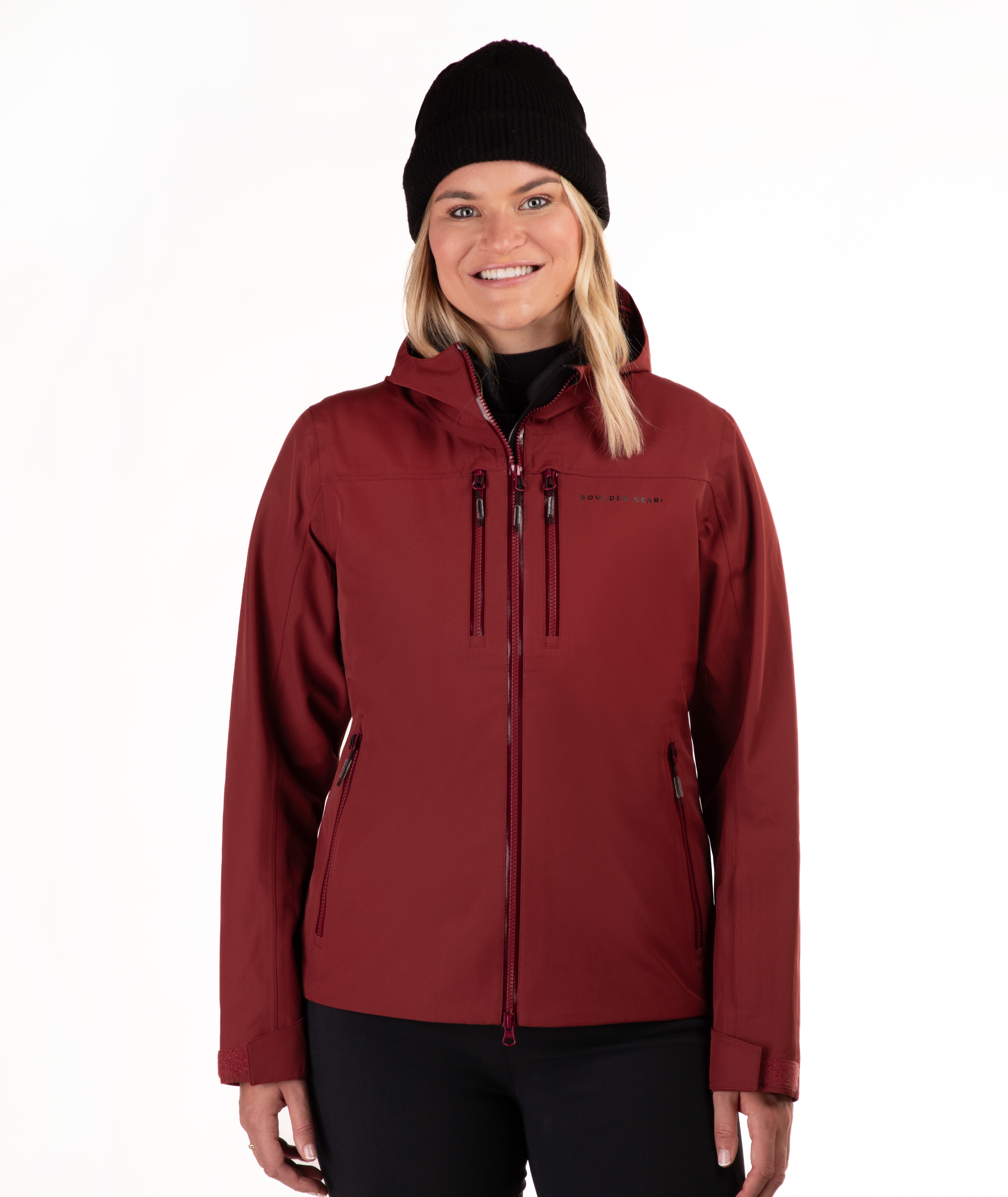 A woman wearing a dark red hooded zip-up jacket, a black beanie, and black pants, standing against a plain white background.