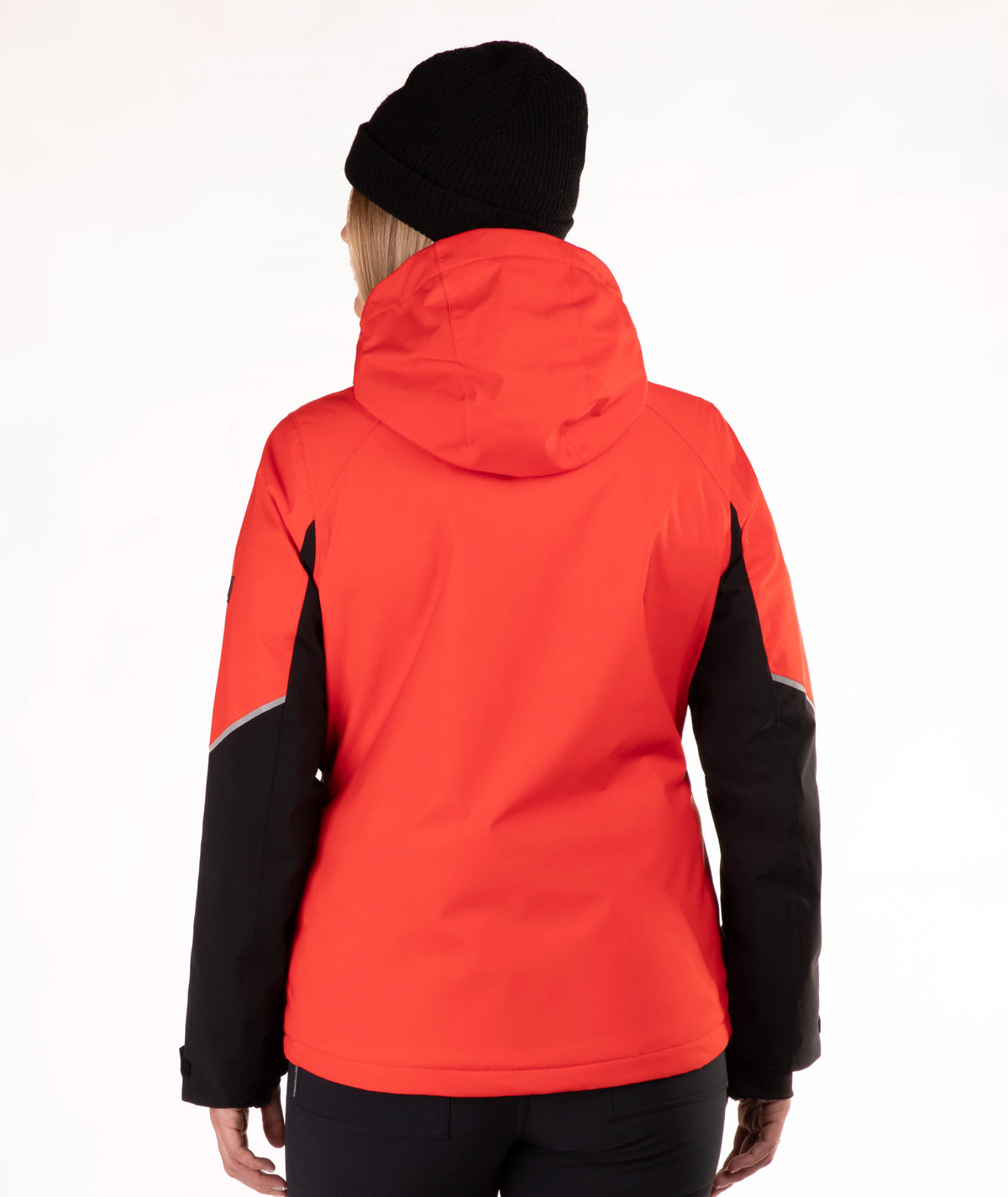 A woman viewed from behind wearing a bright red hooded jacket with black sleeves and a black beanie, against a plain white studio background.
