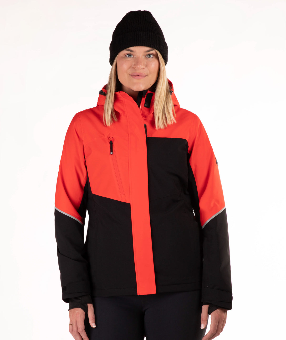 A woman wearing a red and black color-blocked ski jacket, a black beanie, and black pants, standing against a plain white studio background.