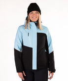 A woman wearing a color-blocked ski jacket in light blue and black, paired with a black beanie, photographed against a plain white studio background.