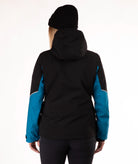 A woman viewed from the back wearing a black hooded jacket with bright blue sleeves, a black beanie, and dark pants against a plain white studio background.