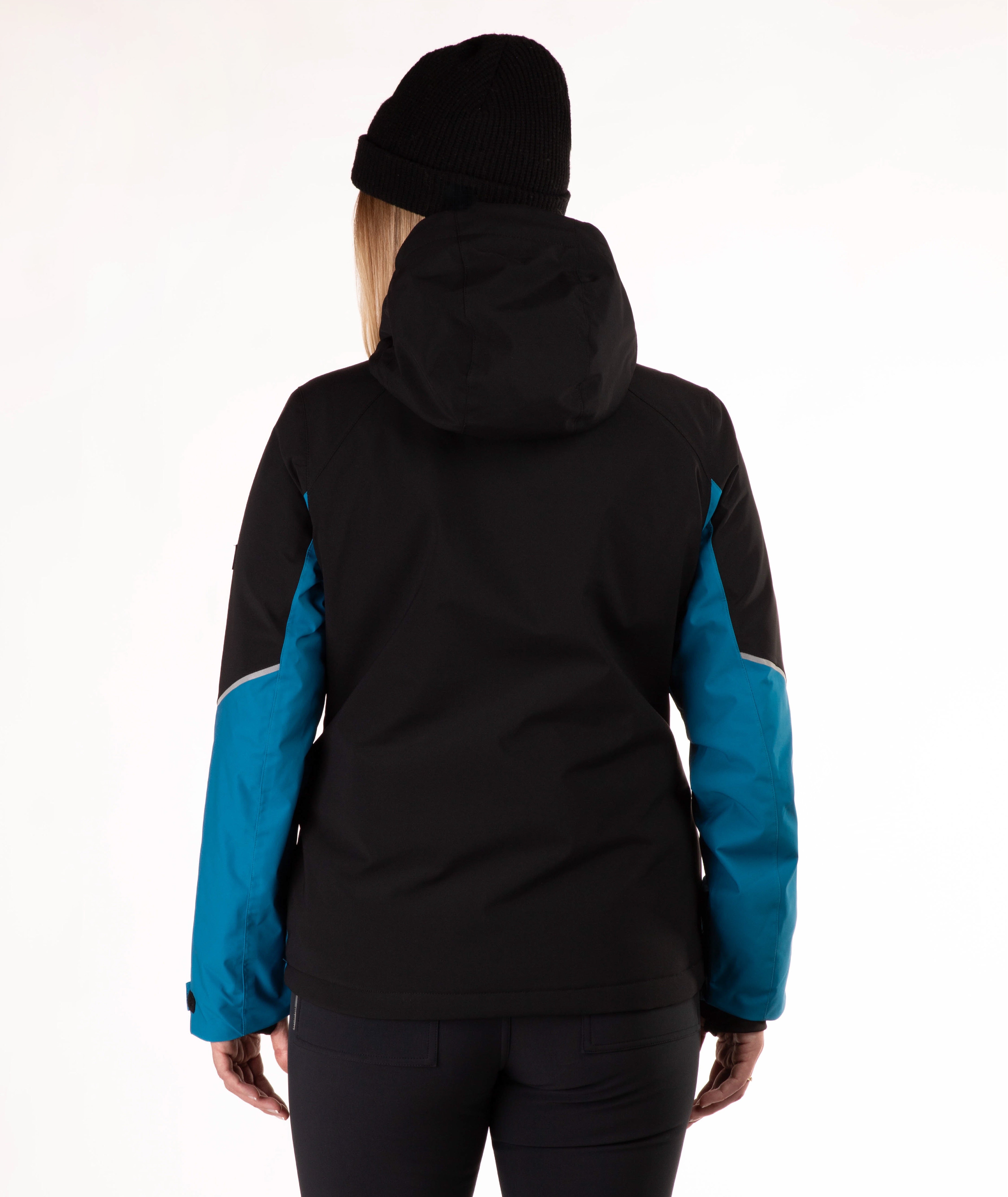 A woman viewed from the back wearing a black hooded jacket with bright blue sleeves, a black beanie, and dark pants against a plain white studio background.