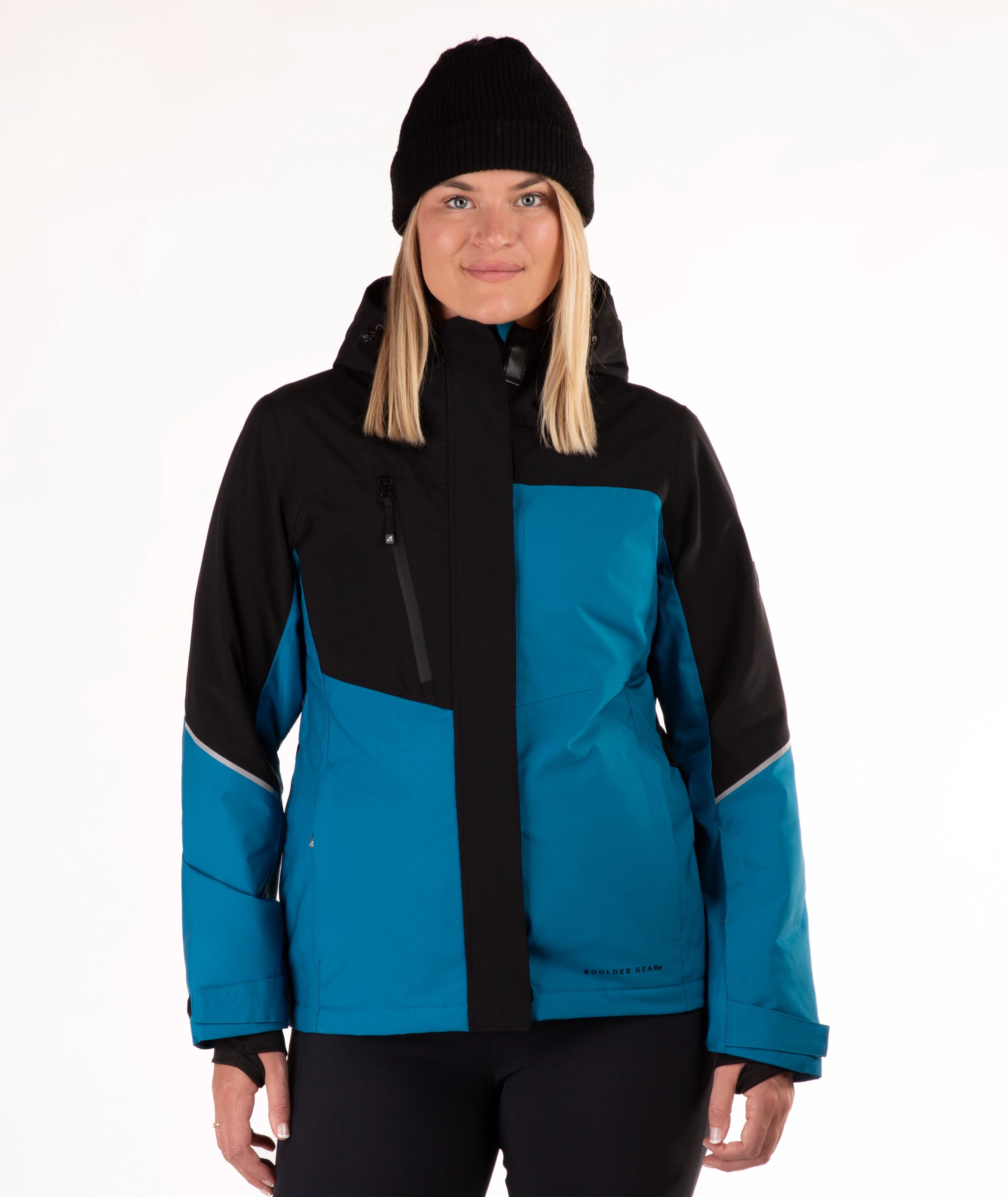 A woman wearing a black and teal color-blocked ski jacket and a black knit beanie, photographed against a plain white studio background.