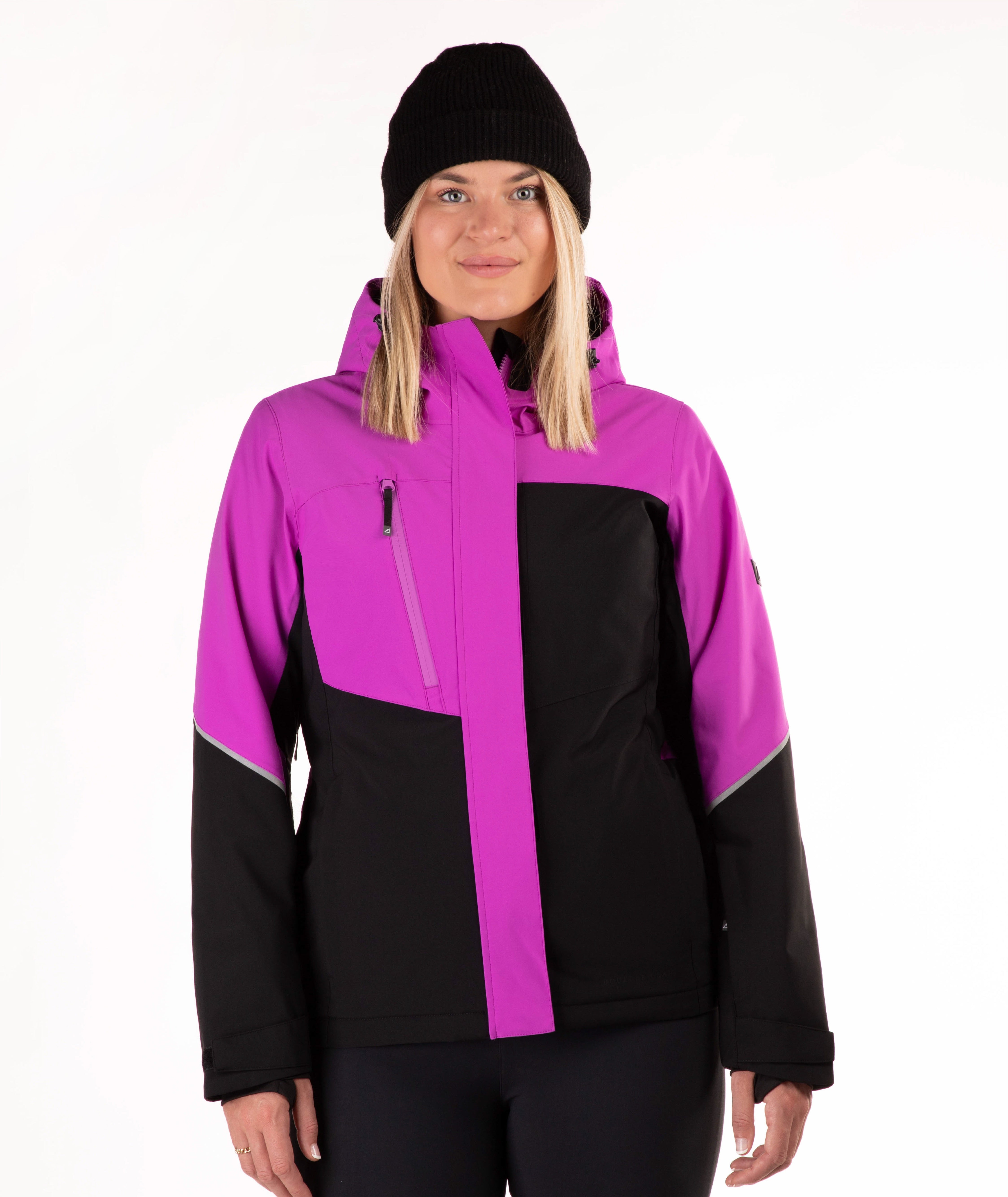 A woman wearing a women's colorblock ski jacket in vibrant magenta and black, paired with a black beanie, photographed against a solid white studio background.