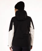 A woman viewed from the back wearing a black hooded jacket with contrasting off-white sleeves, a black beanie, and dark pants against a plain white studio background.