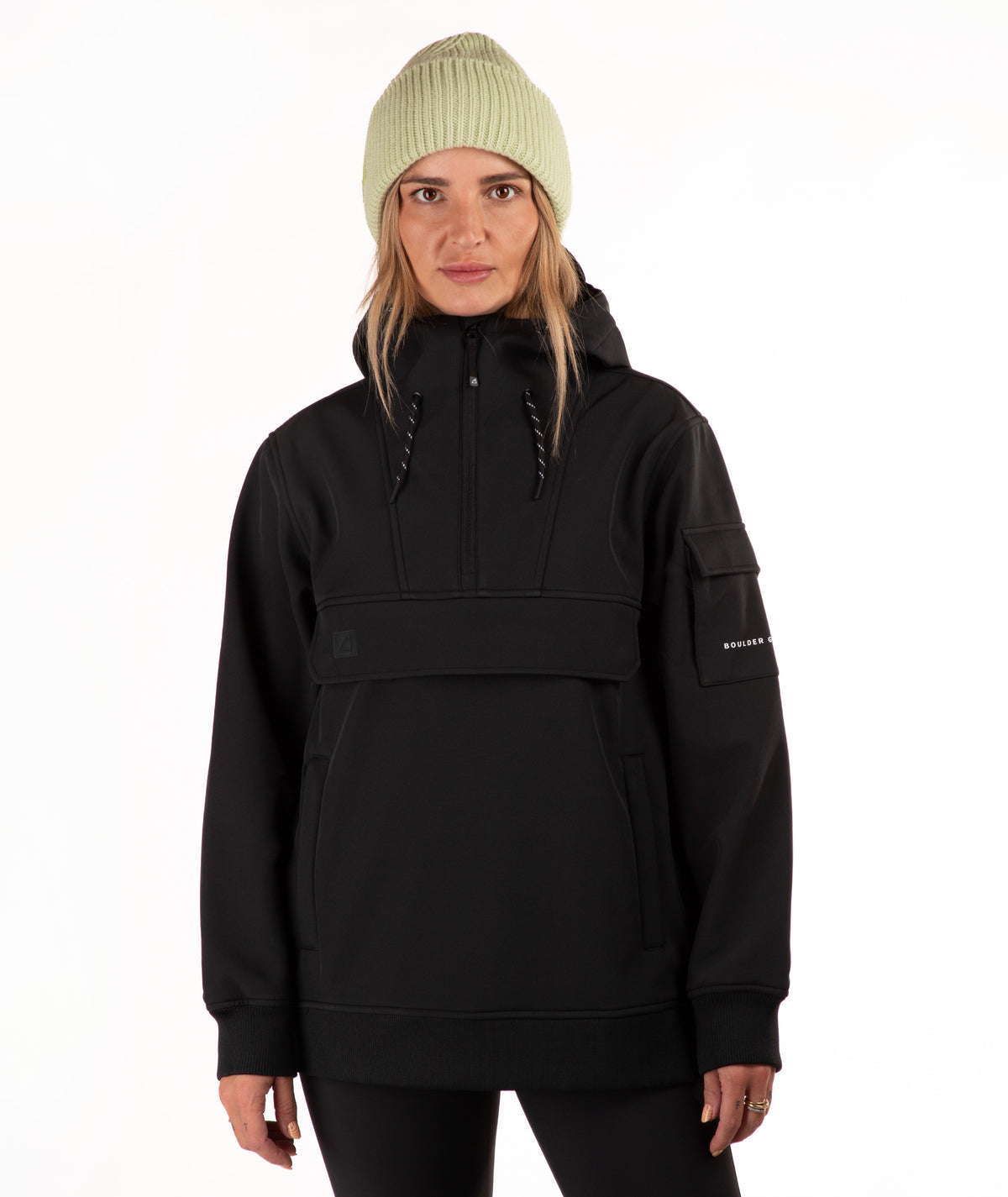 A woman wearing a black half-zip pullover hoodie with a high collar, drawstrings paired with a light green ribbed knit beanie, photographed against a plain white background.