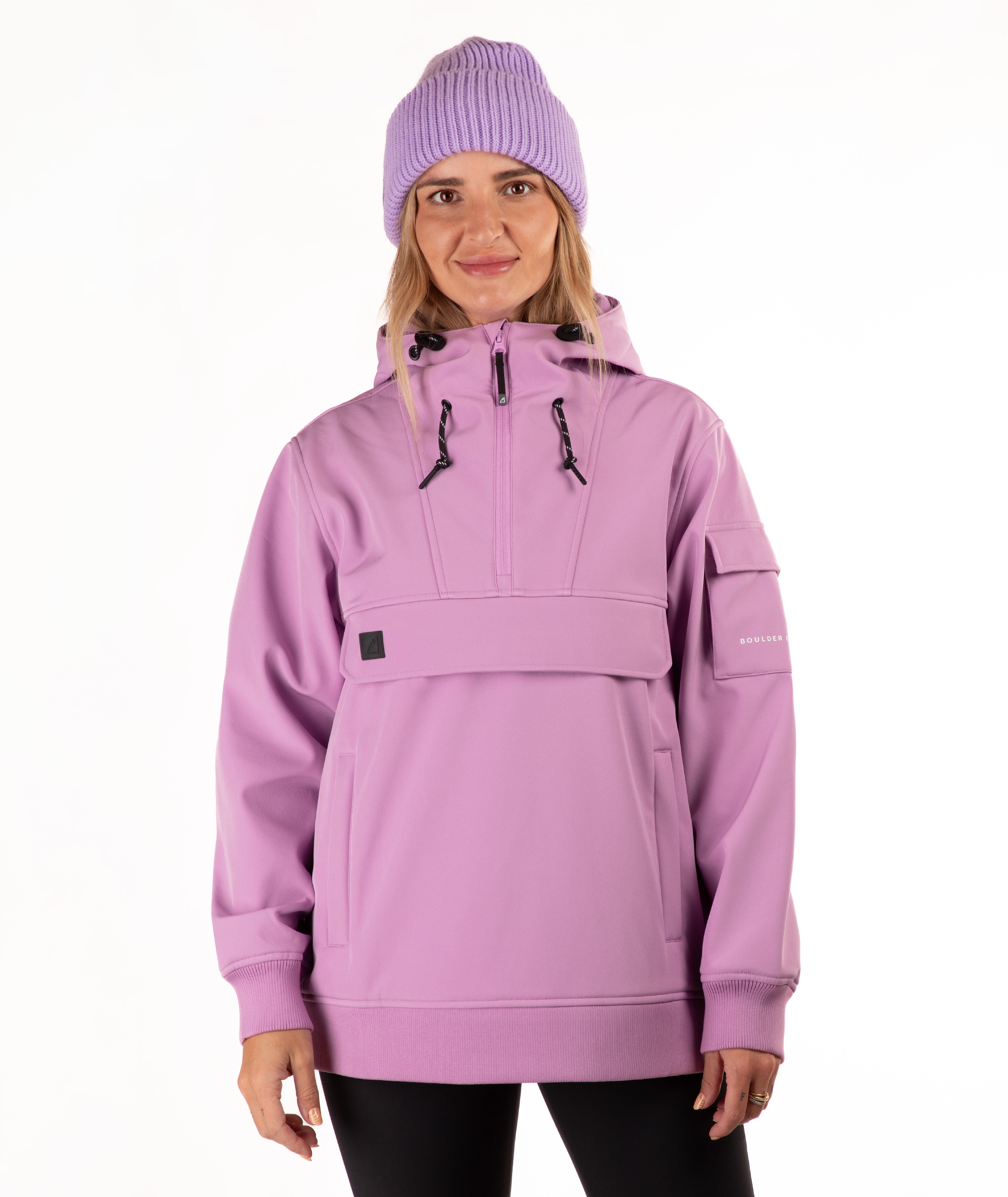A woman wearing a light purple/lavender snowboard jacket with a half-zip hood and a matching knit beanie, photographed against a plain white studio background.