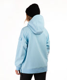 A person shown from the back wearing a light blue hooded jacket and a black beanie against a plain white studio background.