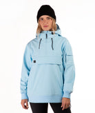 A woman wearing a light blue hooded pullover jacket with a half-zip front, black beanie, and black leggings, photographed against a plain white studio background.