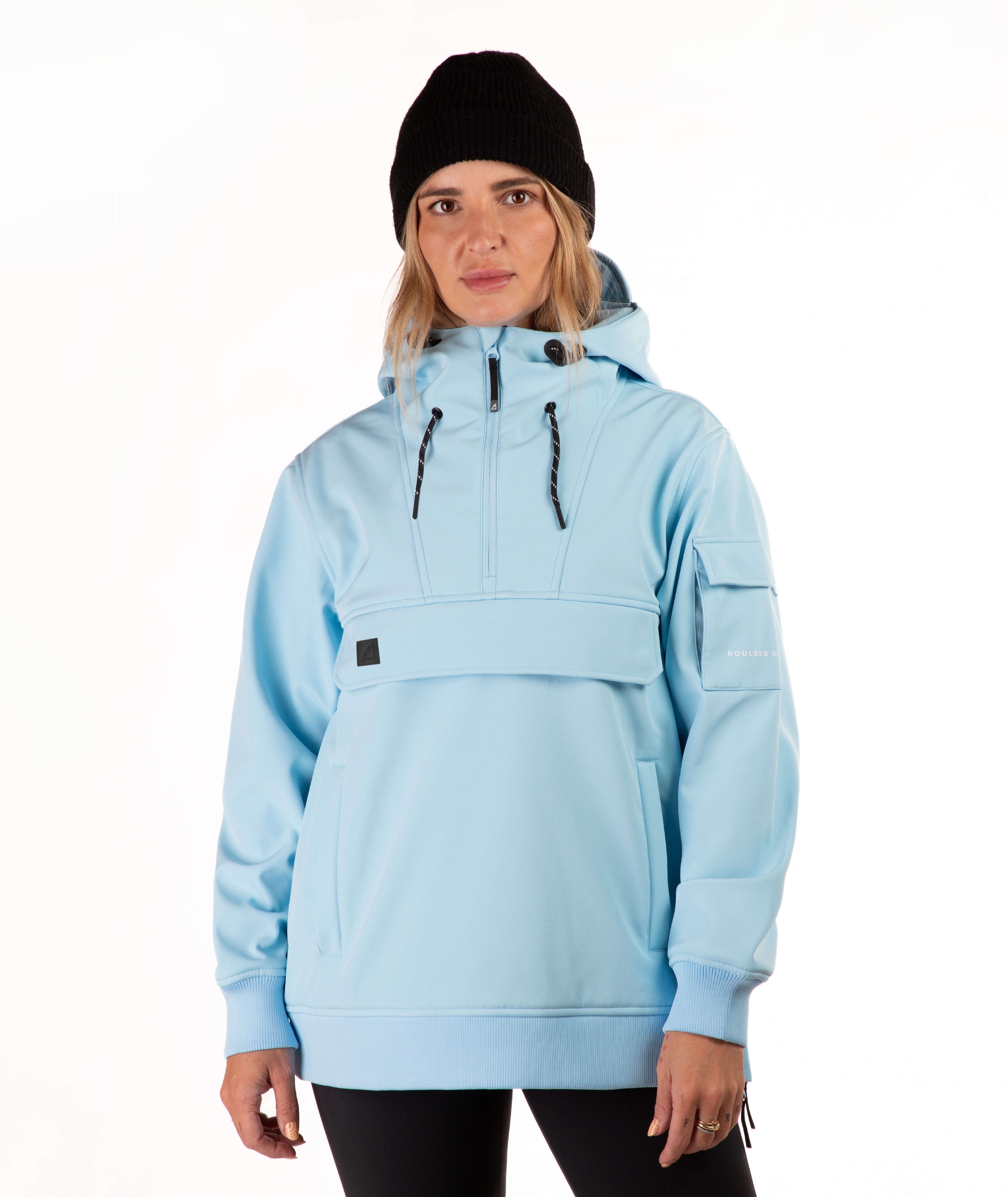 A woman wearing a light blue hooded pullover jacket with a half-zip front, black beanie, and black leggings, photographed against a plain white studio background.