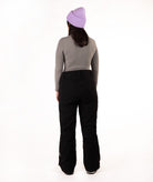A person shown from the back wearing a light purple knit beanie, a gray long-sleeve top, and black ski pants against a plain white studio background.