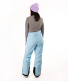 A person shown from the back wearing light blue snow pants, a gray long-sleeve top, and a lavender knit beanie against a plain white studio background.